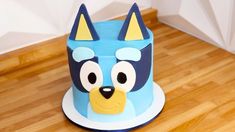 a blue and yellow cake with a dog face on it's side sitting on a wooden floor