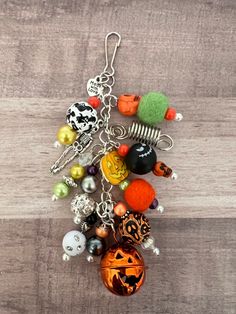 an assortment of halloween themed items hanging from a hook on a wooden surface with beads and charms