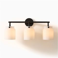 three light bathroom fixture with white glass shades on the top and black metal frame, against a white wall