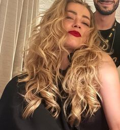 a man standing next to a woman with long blonde hair and red lipstick on her lips