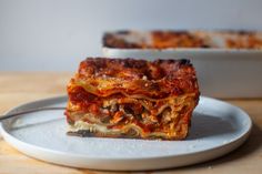 a slice of lasagna on a white plate with a fork next to it