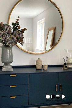 a vase with flowers sitting on top of a blue dresser next to a round mirror