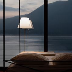 a bed sitting next to a window with a lamp on top of it in front of a lake