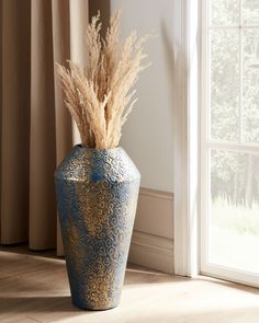 a blue vase sitting on top of a wooden floor next to a window with curtains