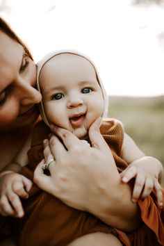 a woman is holding a baby in her lap and smiling at the camera while she holds it up to her face