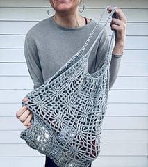 a woman is holding up a crocheted bag in front of a garage door