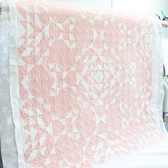 a pink and white quilt is hanging on a rack in front of a window with a chair