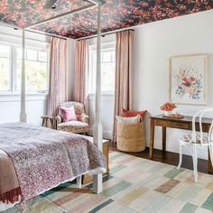 a bed sitting under a canopy in a bedroom next to a table and chairs with flowers on the ceiling