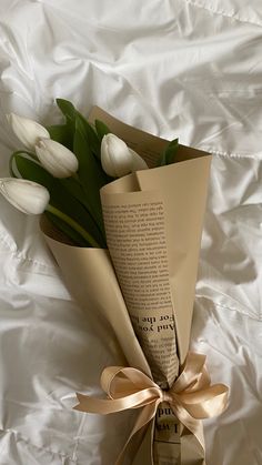 a bouquet of white tulips wrapped in brown paper with a ribbon on top