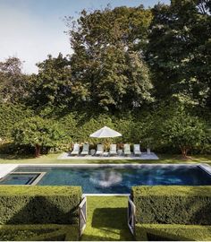 an outdoor pool surrounded by hedges and lawn chairs