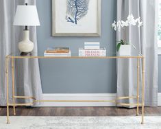 a gold console table with books on it in front of a blue wall and white curtains