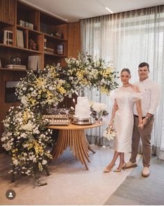 a man and woman standing next to each other in front of a table with flowers