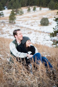 a man and woman are sitting in the tall grass with their arms around each other