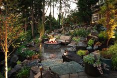 an outdoor fire pit surrounded by trees and rocks in the middle of a garden area