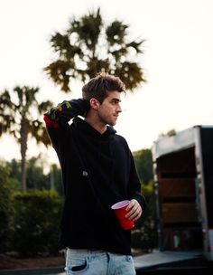 a young man holding a red cup in his left hand while standing next to a truck