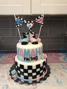 a three tiered cake decorated with black and white checkerboard, pink and blue decorations