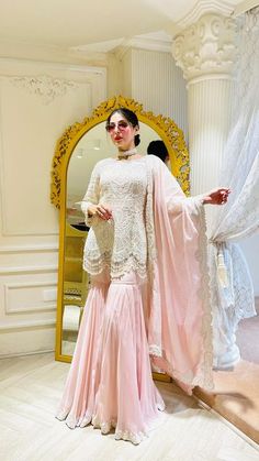 a woman standing in front of a mirror wearing a pink dress and white shawl