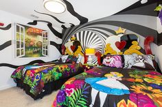 two beds with colorful comforters in a white room decorated with black and white wallpaper