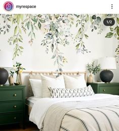 a bed with white sheets and pillows in front of a wall mural that has green leaves on it