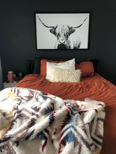 a bed with an orange bedspread and a cow painting on the wall