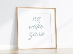 a white framed print with the words no wake zone on it in grey ink, against a plain white wall