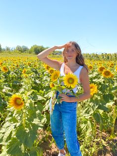 a woman standing in a sunflower field with her hands on her head and looking at the camera