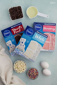 the ingredients to make this cake are laid out on a blue tablecloth and include eggs, marshmallows, brownies, chocolate chips, frosting