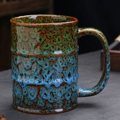 a blue and green coffee mug sitting on top of a table next to a piece of wood