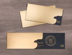 two gold business cards on top of a wooden table next to a black and white envelope