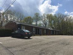 an empty parking lot with a car parked in front of the building and trees behind it