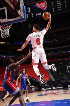 a basketball player jumping up to dunk the ball in front of two other players