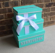 three stacked boxes with white bows on the top and bottom, sitting in front of a brick wall