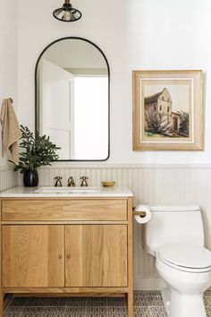 a white toilet sitting next to a wooden cabinet in a bathroom under a large mirror