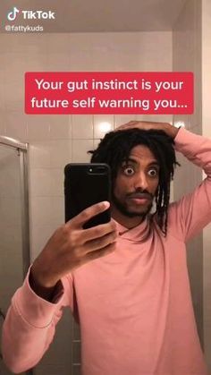 a man with dreadlocks taking a selfie in the bathroom while holding his cell phone