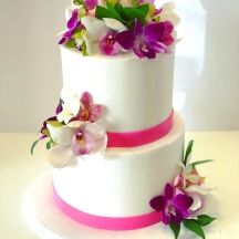 a three tiered white cake with purple and pink flowers on it's side