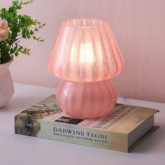 a pink lamp sitting on top of a book next to a vase with flowers in it