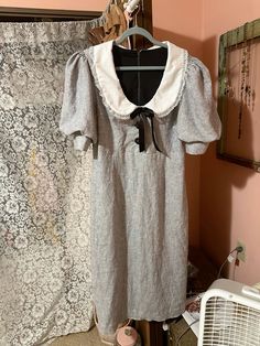 a dress hanging on a clothes rack in front of a wall with an old curtain