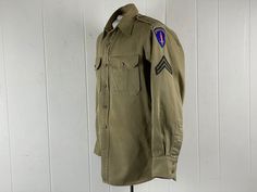 "Vintage 1940s WWII U.S. Army military shirt. Made khaki cotton. Has two button down pockets, button down front, shoulder epaulets, side gussets, button cuffs and three patches. Has a tailored fit. About a size medium. Actual measurements are:   46\" around the chest   42\" around the waist  46\" hips   18\" shoulder seam to shoulder seam  23\" shoulder seam to cuff  30\" overall length  In good condition with some pin holes in the collar and slight variance in the color (patina)" Retro Khaki Button-up Shirt, Khaki Military Collared Shirt, Khaki Collared Military Shirt, Vintage Khaki Button-up Shirt, Vintage Collared Khaki Shirt, Vintage Khaki Shirt With Button Closure, Shirt With Patches, Army Shirt, Military Shirt