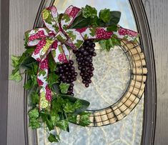 a grape wreath with green leaves and red berries on a door hanger in front of a glass window