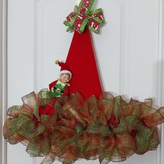 the elf is sitting on top of the christmas tree door hanger in front of the door