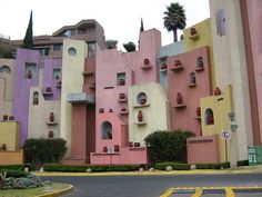 an unusual building with many windows and plants on the outside, in front of a parking lot