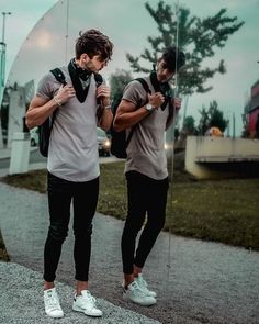 two young men standing next to each other in front of a large mirror with their reflection on it