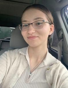 a woman sitting in the back seat of a car wearing glasses and a white shirt