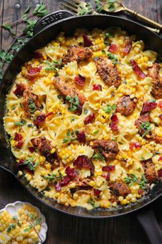 a skillet filled with pasta and meat on top of a wooden table next to silverware