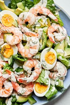 a salad with shrimp, avocado and boiled eggs in it on a blue plate