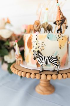 a zebra figurine is standing on top of a birthday cake with other toy animals in the background