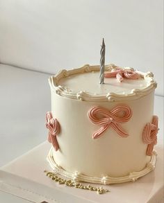 a white cake with pink bows and a single candle