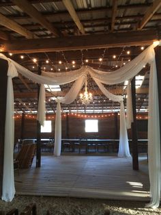 the inside of a barn decorated with white drapes and lights