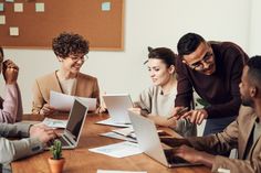 a group of people sitting around a wooden table with laptops in front of them