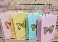 four paper bags with butterflies on them are lined up against a wooden wall, one is pink and the other is blue